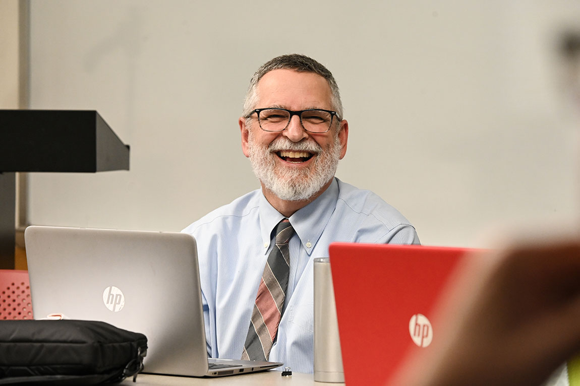 An instructor with glasses and a beard smiles as he teaches class